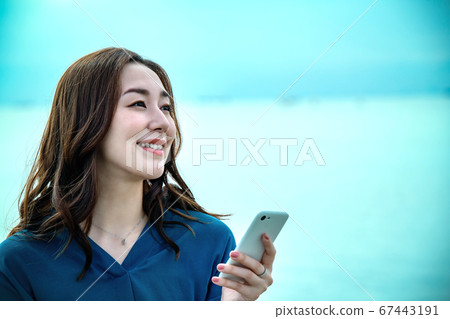A young woman standing in the sea operating a smartphone A young woman standing in the sea operating a smartphone 67443191