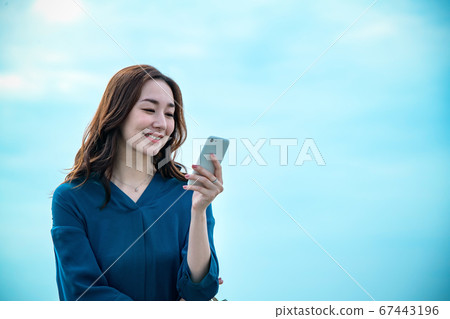 站立在海的一個少婦操作智能手機 站立在海的一個少婦操作智能手機 67443196