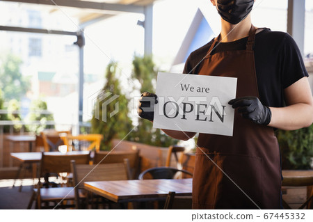 The waiter works in a restaurant in a medical mask, gloves during coronavirus pandemic 67445332