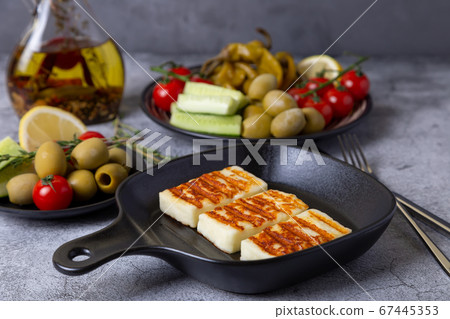 Grilled haloumi cheese on a black pan with olives, tomatoes, cucumbers and pepperoni. Close-up. 67445353
