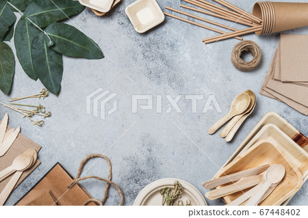 Eco craft paper and wooden tableware. Paper cups, dishes, bag, plates and bamboo cutlery on gray background. Recycling or eco-friendly concept, Top view, Copy space Eco craft paper and wooden tableware. Paper cups, dishes, bag, plates and bamboo cutlery on gray background. Recycling or eco-friendly concept, Top view, Copy space 67448402