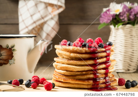 Stack of pancakes with berries, poured with syrup on a wooden table in a rustic style 67448798