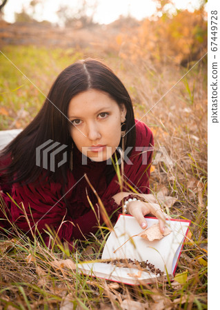 Serious girl in lying in tall grass in the fields with poetry book, she is looking at camera seriously Serious girl in lying in tall grass in the fields with poetry book, she is looking at camera seriously 67449728