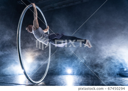 Cyr Wheel circus artist on smoked, dark background performing on stage Cyr Wheel circus artist on smoked, dark background performing on stage 67450294