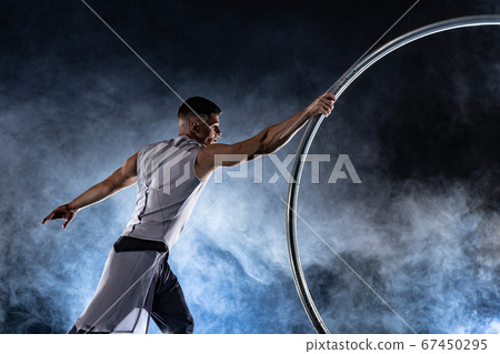 Cyr Wheel circus artist on smoked, dark background performing on stage  67450295