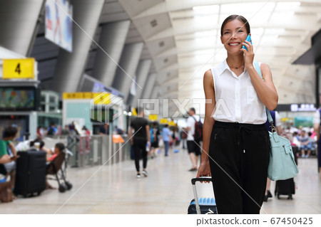 Businesswoman on commute transit talking on the smartphone while walking with hand luggage in train station or airpot going to boarding gate. Asian woman happy using mobile phone app for conversation Businesswoman on commute transit talking on the smartphone while walking with hand luggage in train station or airpot going to boarding gate. Asian woman happy using mobile phone app for conversation 67450425