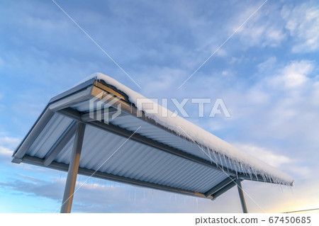 Roof with snow and icicles against cloudy blue sky Roof with snow and icicles against cloudy blue sky 67450685