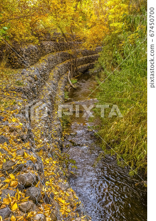 Rocky stream bank with mesh wire and golden leaves 67450700