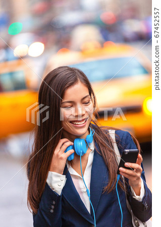 Headphones young woman walking in new york city using phone app listening to podcast or audiobook with earphones commuting from work. Asian girl businesswoman using cellphone Headphones young woman walking in new york city using phone app listening to podcast or audiobook with earphones commuting from work. Asian girl businesswoman using cellphone 67452557