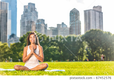 New York City Central Park yoga girl relaxing meditating woman in meditation in outside in summer. Beautiful young mixed race Asian Caucasian model sitting in lotus pose in grass 67452576