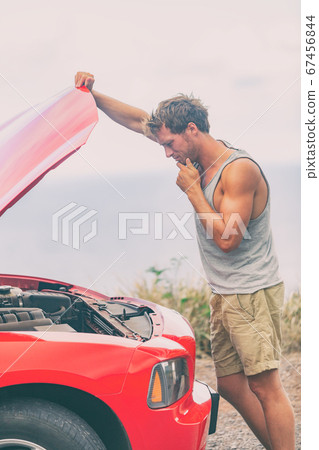 Car breakdown problem. Road trip travel young man on side of the road with broken engine looking at motor in open hood repairing issue Car breakdown problem. Road trip travel young man on side of the road with broken engine looking at motor in open hood repairing issue 67456844