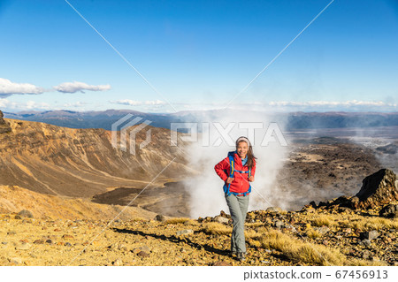 New Zealand Tongariro Alpine Crossing Hiking trek hiker woman with bag and outdoor jacket tramping in volcanic steam vents fumaroles background. Summer travel vacation adventure trekking girl hike 67456913