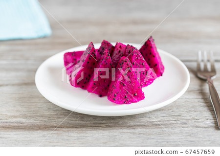 Sliced pink dragon fruit on white ceramic plate on vintage wooden table, selective focus 67457659