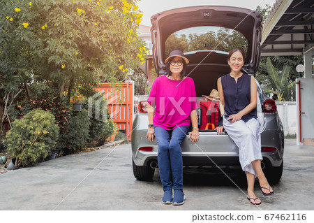 Two women senior mother and daughter sitting in back of the car, with suitcases on car trip. 67462116