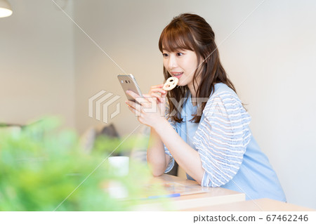 Young woman looking at smartphone while biting cookies in cafe 67462246