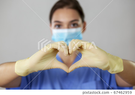 Female nurse in a face mask makes the heart shape with her fingers in gloves. 67462959