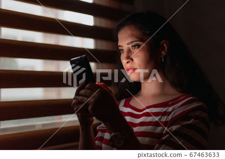 Young and serious woman looking smartphone in dark room. 67463633