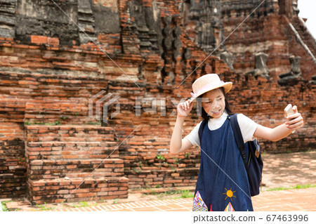Cute happy smiling tourist girl taking self-portrait picture with smartphone at Wat Chaiwatthanaram is a Buddhist temple in the city of Ayutthaya Historical Park,Thailand, summer vacation,travel conce 67463996