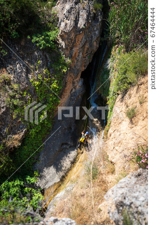 Unrecognizable person canyoning with ropes under the stream 67464444