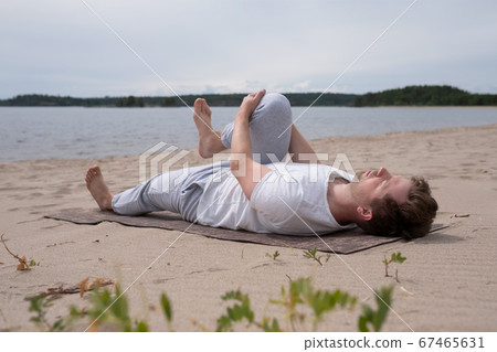 Young man practicing yoga pavanamuktasana outdoors on the beach 67465631