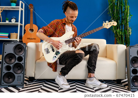 Young caucasian man with dreadlocks playing electric guitar in his room 67470415