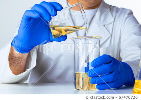Scientist or doctor in blue gloves pouring some yellow liquid into a flask 67470726