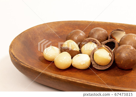 Macadamia nuts with shells on a wooden plate 67473815