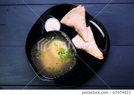 Fresh fish soup with egg in a black deep dish with pancakes and sour cream on a black background, top view. Blue wooden background Fresh fish soup with egg in a black deep dish with pancakes and sour cream on a black background, top view. Blue wooden background 67474815