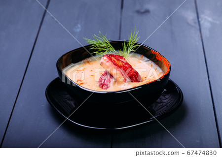 Cream soup with pieces of fish or salmon fillet in a black dishes on a wooden table Cream soup with pieces of fish or salmon fillet in a black dishes on a wooden table 67474830