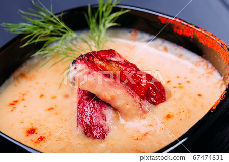 Cream soup with pieces of fish or salmon fillet in a black dishes on a wooden table. chinese food, soup. Front view Cream soup with pieces of fish or salmon fillet in a black dishes on a wooden table. chinese food, soup. Front view 67474831