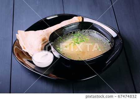 Fresh fish soup with egg in a black deep dish with pancakes and sour cream on a black background, front view. Blue wooden background 67474832