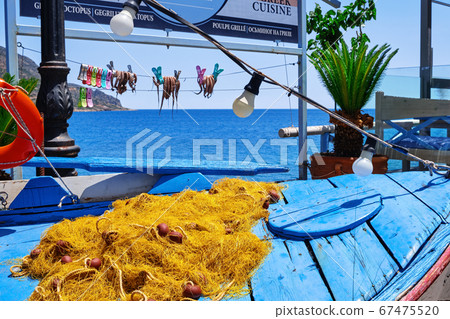 Outdoor display, traditional fisherman boat, fishing net, sun-dried octopuses on rope, blue sea and typical Greek hills in background, Crete, Greece Outdoor display, traditional fisherman boat, fishing net, sun-dried octopuses on rope, blue sea and typical Greek hills in background, Crete, Greece 67475520