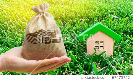 Miniature wooden house and money bag on grass. Real estate concept. Eco-friendly and energy efficient house. Buying a home outside the city. The urban downshift. Nature. Fresh air. Mortgage, loan. Miniature wooden house and money bag on grass. Real estate concept. Eco-friendly and energy efficient house. Buying a home outside the city. The urban downshift. Nature. Fresh air. Mortgage, loan. 67475742