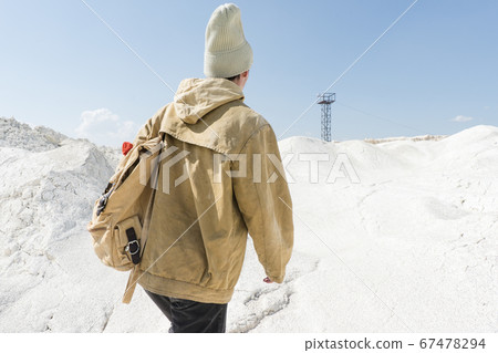 a man with a backpack walks along the white sand towards an abandoned old iron tower a man with a backpack walks along the white sand towards an abandoned old iron tower 67478294