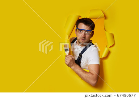worker in safety glasses and uniform holding paint brush 67480677