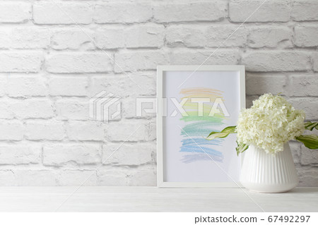 An abstract picture frame stands the will of a white brick wall. Green hydrangea in a vase in the Nordic style. An abstract picture frame stands the will of a white brick wall. Green hydrangea in a vase in the Nordic style. 67492297