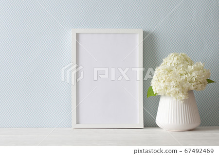 A bouquet of white hydrangea stands near the blue wall on a wooden table. A4 frame stands upright. Bundle. 67492469