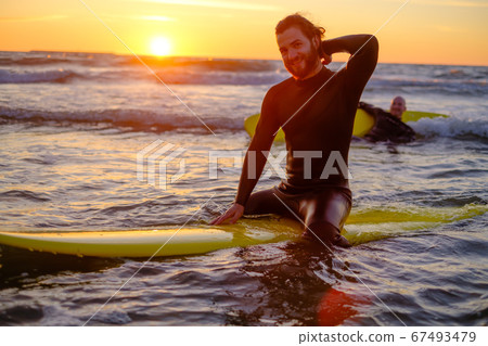 Surfer sitting on surfboard in sea Surfer sitting on surfboard in sea 67493479