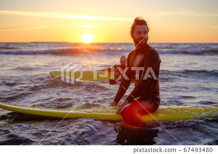Surfer sitting on surfboard in sea 67493480