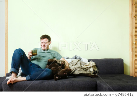 Happy handsome man sitting on the couch at home with pet dog labrador retriever 67495412