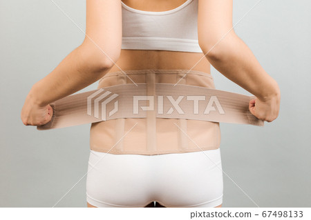 Close up of supporting bandage against backache on pregnant woman in  underwear at gray background with copy space. Mother is suffering from pain  in the back. Orthopedic abdominal support belt concept Photos