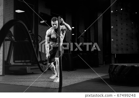 Monochrome portrait of shirtless man training with ropes. 67499248