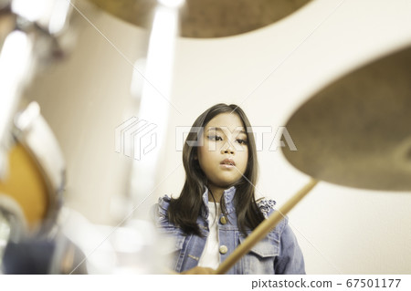 A cute Asian elementary school girl with long hair and wearing jeans playing a drum  67501177