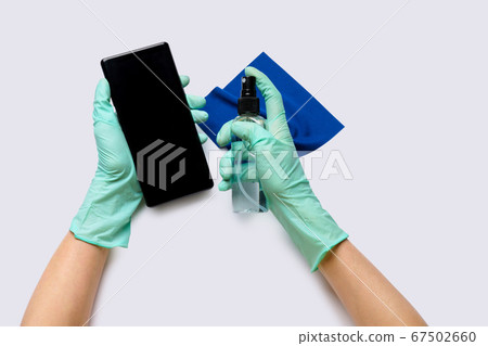 Female's hands in latex gloves wiping mobile phone with alcohol decontaminating agent top view over light grey background Female's hands in latex gloves wiping mobile phone with alcohol decontaminating agent top view over light grey background 67502660