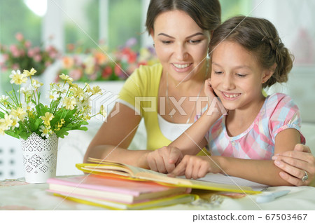Little cute girl reading book with mother at the table at home Little cute girl reading book with mother at the table at home 67503467