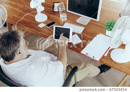 Businessman, manager in office with computer and fan cooling off, feeling hot, flushed 67503854