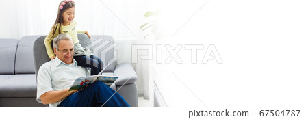 Grandfather and granddaughter on sofa at home. Grandpa and children are watching photos in album. 67504787