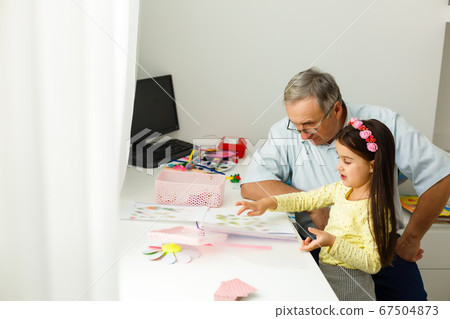 Caring grandfather doing home assignment together with granddaughter Caring grandfather doing home assignment together with granddaughter 67504873