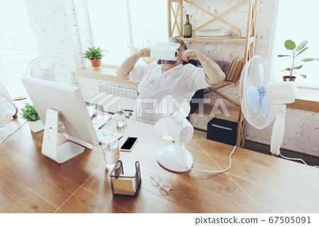 Businessman, manager in office with computer and fan cooling off, feeling hot, flushed Businessman, manager in office with computer and fan cooling off, feeling hot, flushed 67505091