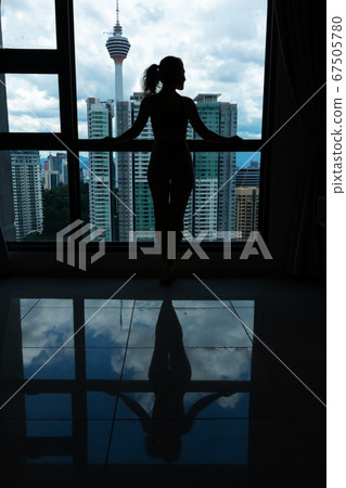 A slender girl is looking at the city through a 67505780